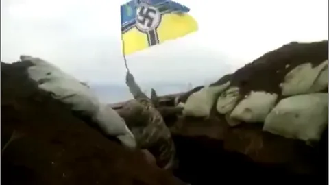 A screenshot from a video clip - Ukrainian soldier waving a swastika flag in a trench